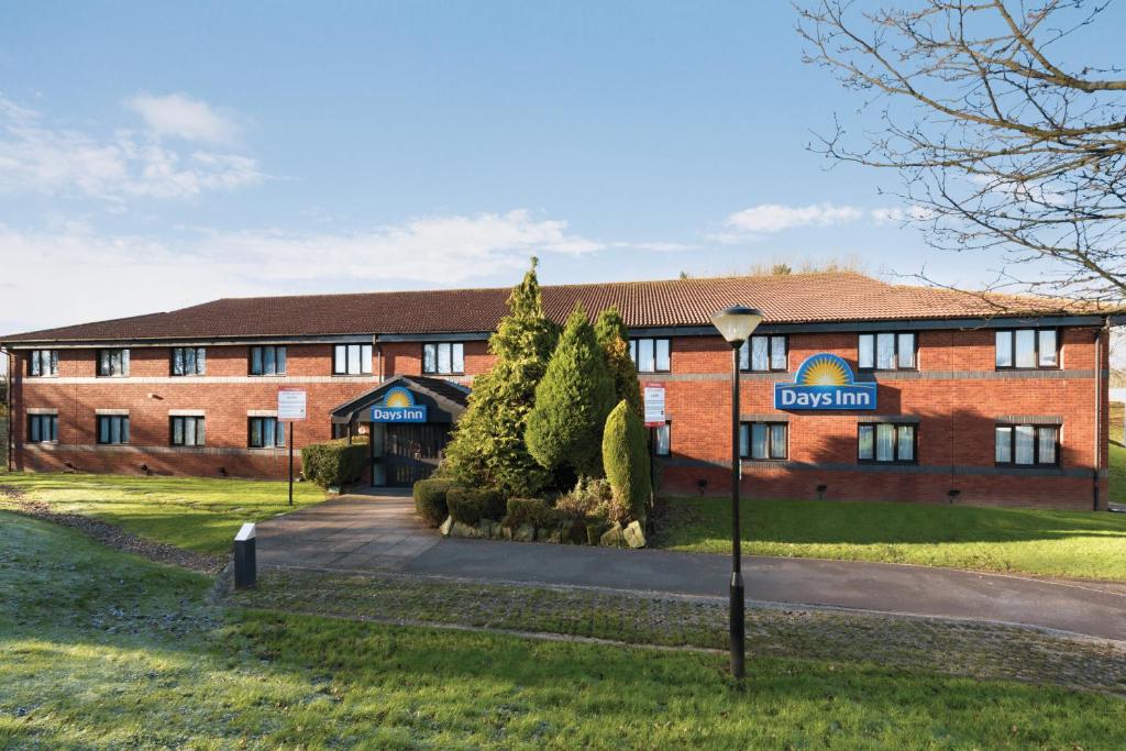 Days Inn Hotel Membury في Lambourn: مبنى من الطوب الأحمر مع علامة أمامه