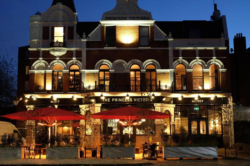 un bâtiment avec des tables et des parasols devant lui dans l'établissement The Princess Victoria, à Londres