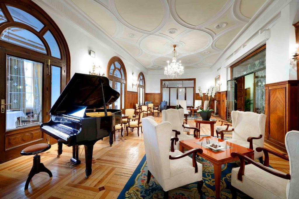 a living room with a piano and a dining room at Exe Victoria Palace in San Lorenzo de El Escorial
