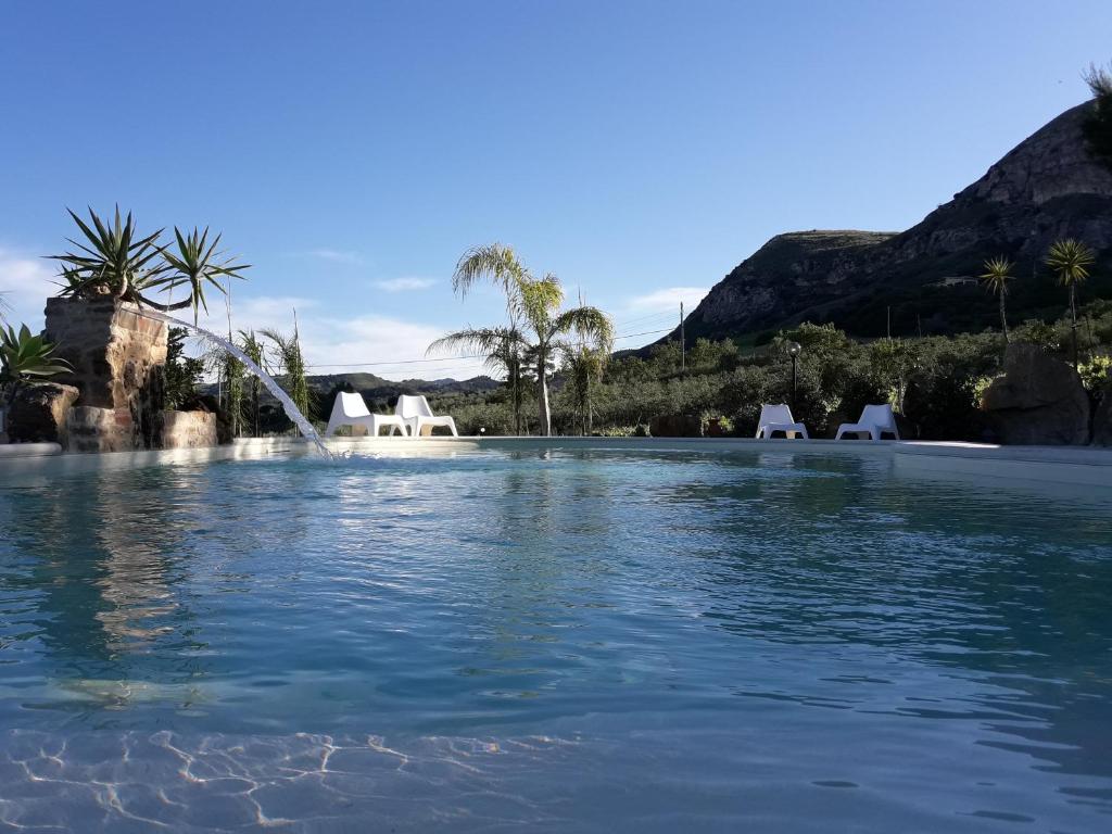una piscina de agua con sillas y montañas al fondo en La Suite Di Segesta en Calatafimi