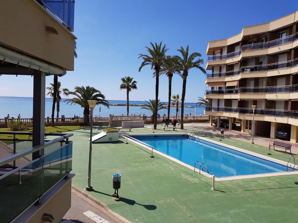 a swimming pool with palm trees and a building at Apartamento Sol de España in Cambrils