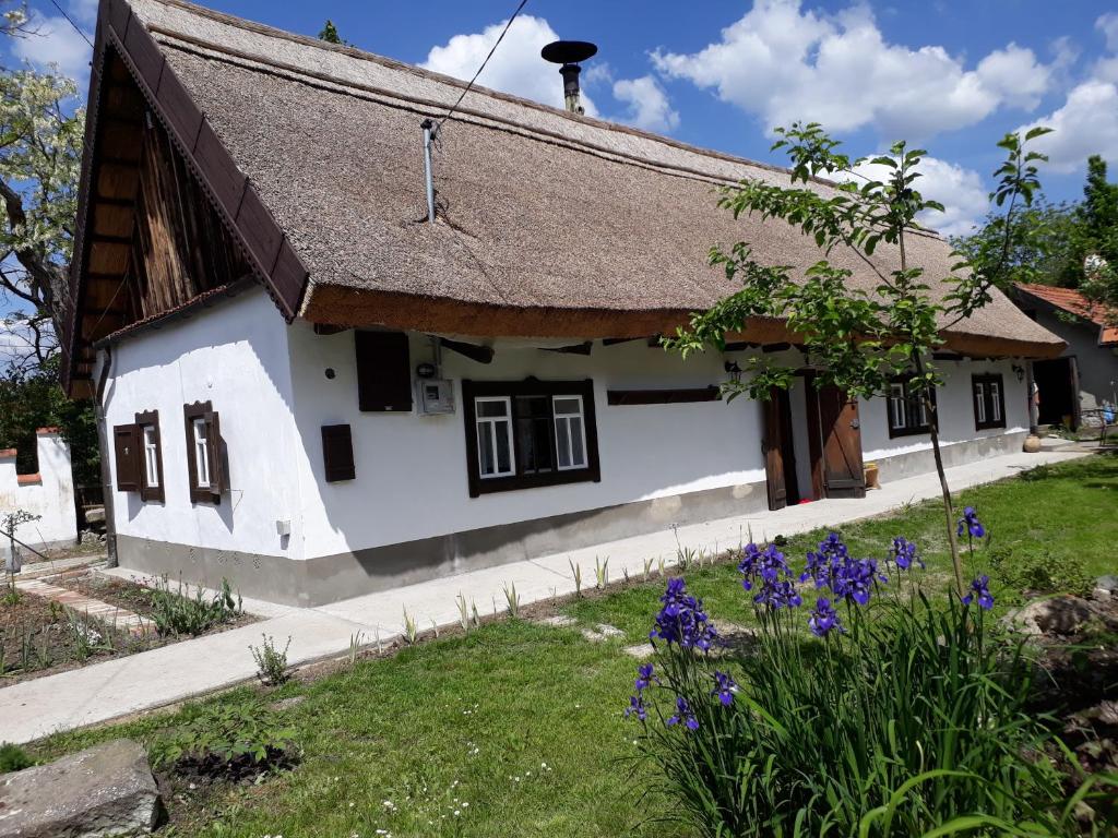 a white cottage with a thatched roof and purple flowers at Forrás in Egerszólát