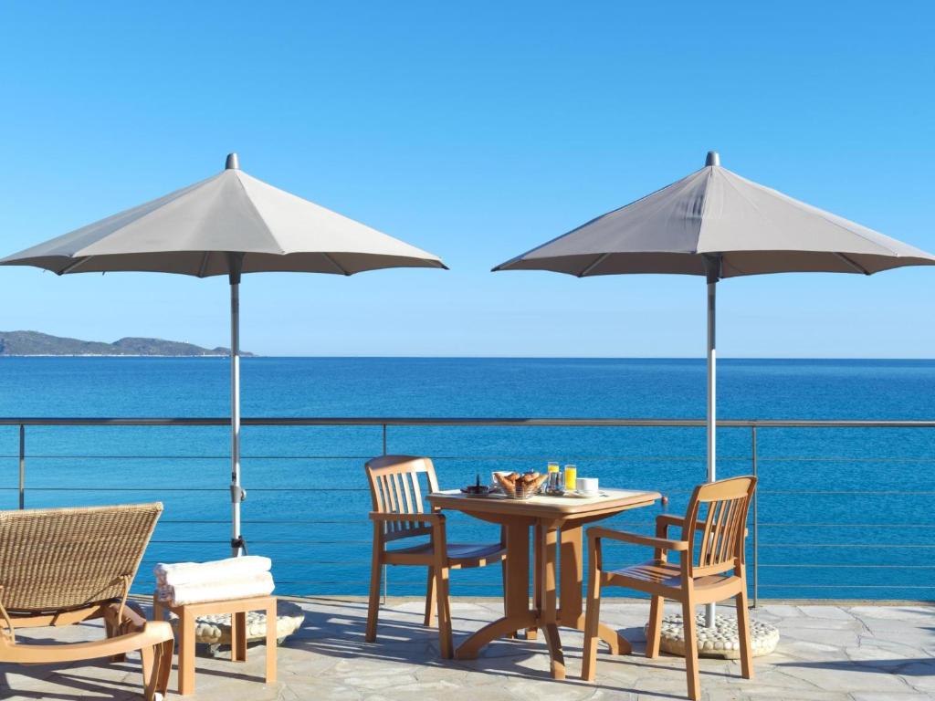 a table and chairs with umbrellas and the ocean at Hôtel Dolce Notte in Saint-Florent