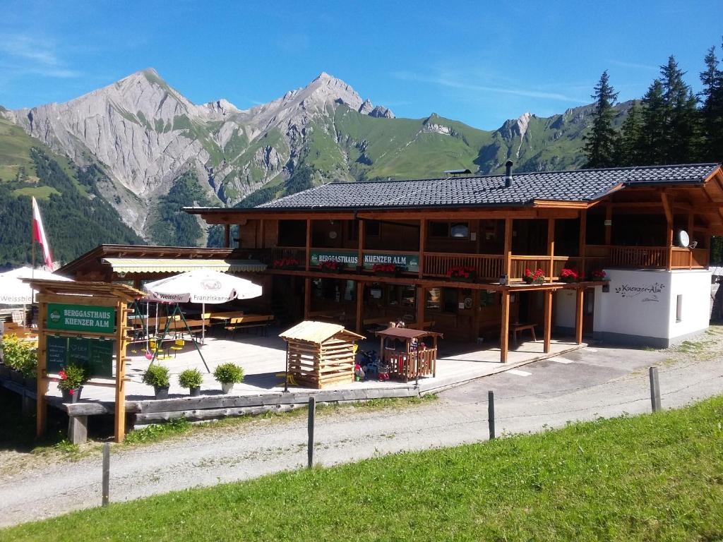 een groot houten gebouw met bergen op de achtergrond bij Ferienwohnung Kuenzer Alm in Matrei in Osttirol