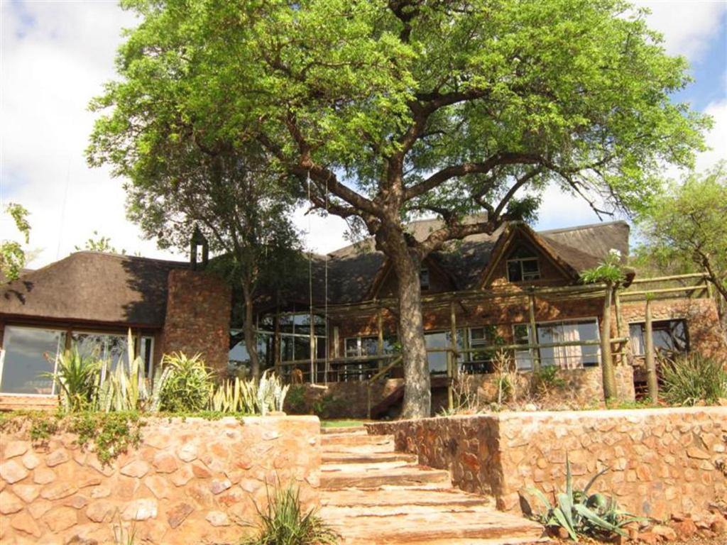 una casa con un árbol y una pared de piedra en Marula Cottage Guest Lodge, en Thabazimbi