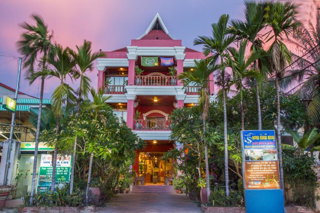 a pink building with palm trees in front of it at Side Walk Hotel in Siem Reap