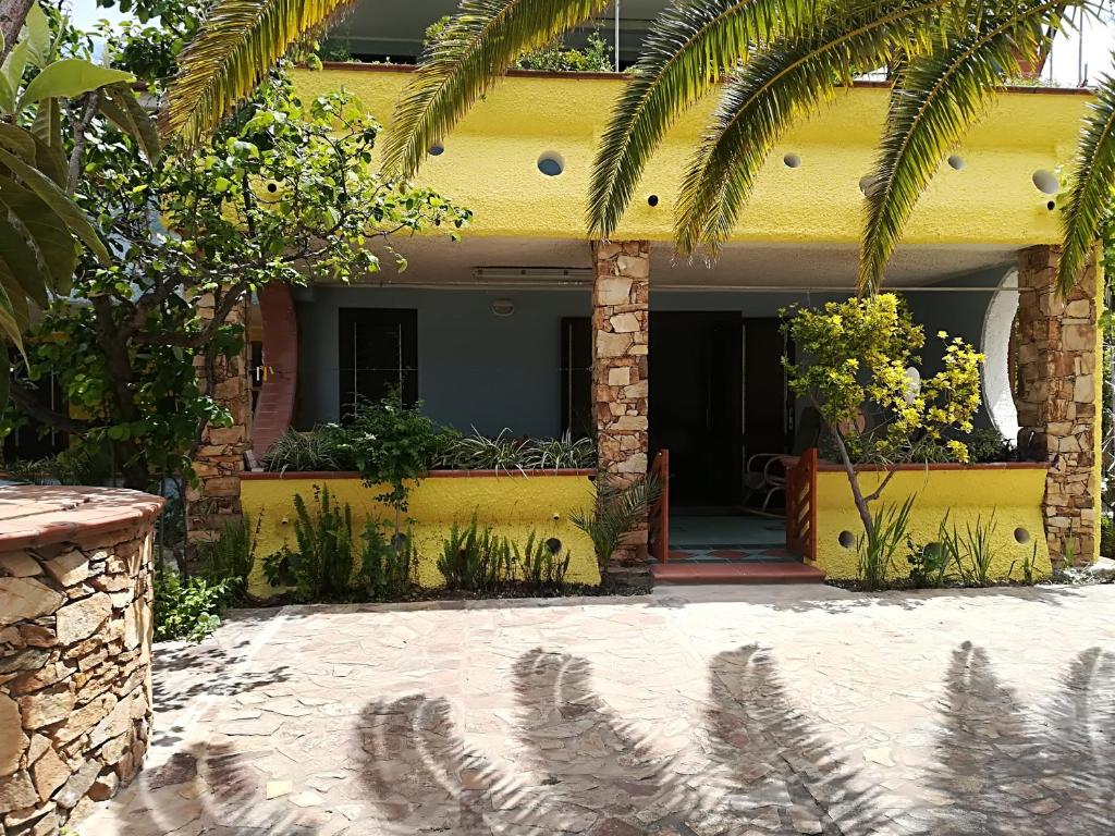 een geel huis met palmbomen ervoor bij Casa Bandinu in Budoni