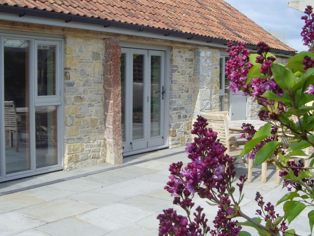 una casa de piedra con puertas de cristal y flores púrpuras en Pear Tree Cottages, en Wedmore