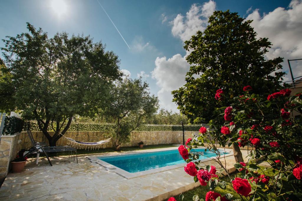 a swimming pool in a yard with a tree and roses at Holiday home Vitali in Kaštela