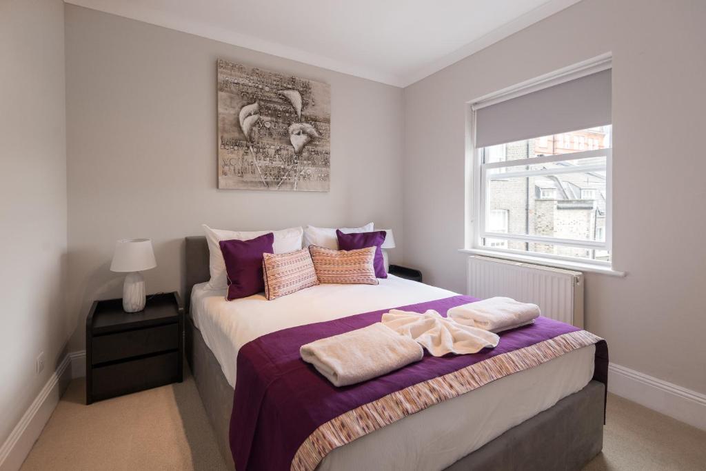 um quarto com uma cama com lençóis roxos e uma janela em One bedroom High street kensington Apartment em Londres