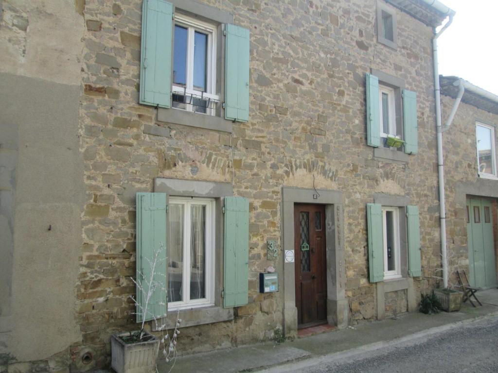 a stone building with green shutters and a door at Epicerie de Lili in Pradelles-en-Val