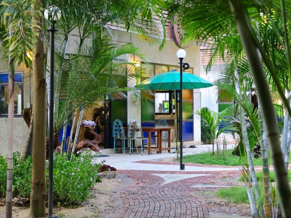 um guarda-chuva verde em frente a um edifício com palmeiras em The Picturebook Guesthouse em Mae Sot