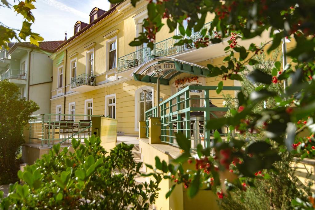 un grand bâtiment jaune avec des balcons et des arbres dans l'établissement Hotel Spa Hévíz, à Hévíz
