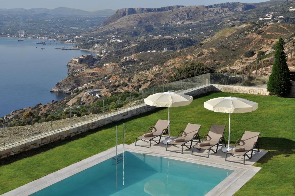 a pool with chairs and umbrellas on a hill at Ocean Villas Complex in Agia Pelagia