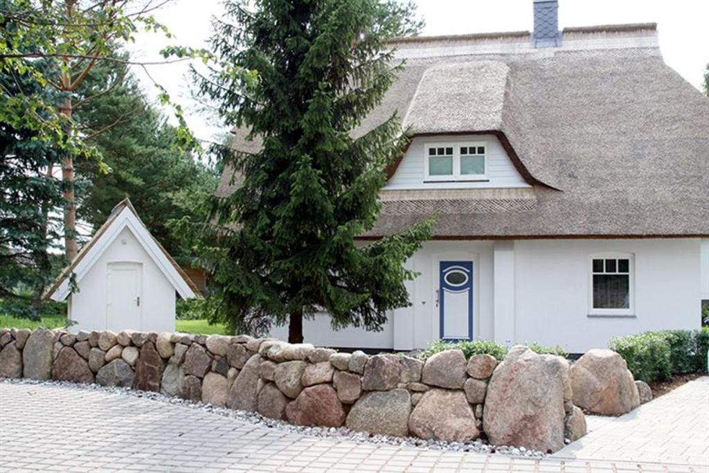 una casa blanca con una valla de piedra delante de ella en Idylle unterm Reet - Reetdachhäuser am Walde, en Trassenheide