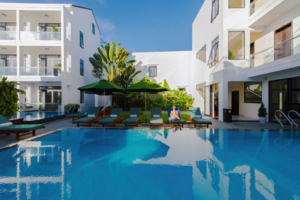 una piscina con sillas y sombrillas junto a un edificio en Banana Garden Villa, en Hoi An