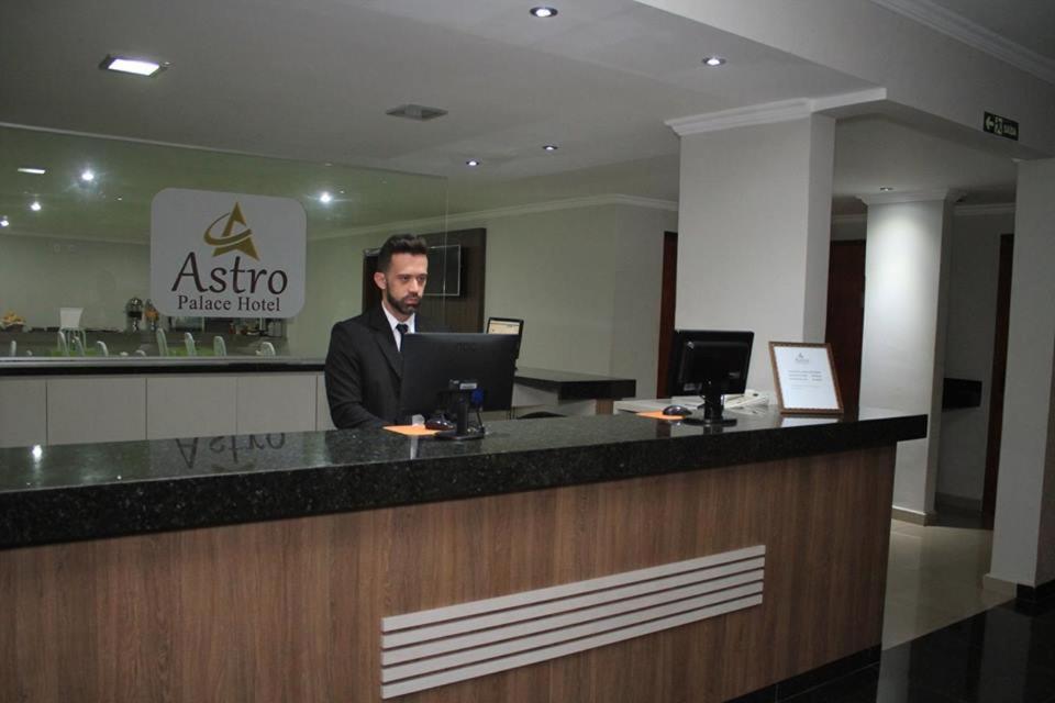 a man in a suit sitting at a counter with a laptop at Astro Palace Hotel in Uberlândia