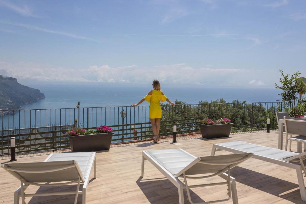 a woman in a yellow dress standing on a balcony overlooking the ocean at Angiem Holiday House Ravello in Ravello