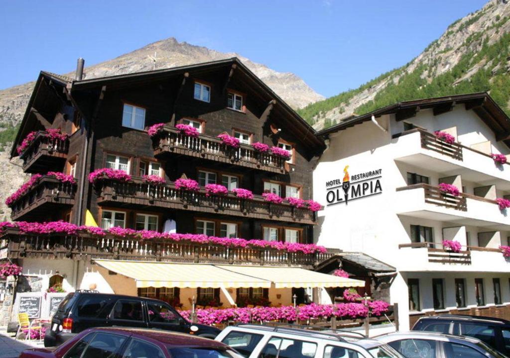 a large building with flowers on the balconies in a parking lot at Hotel Olympia in Saas-Almagell