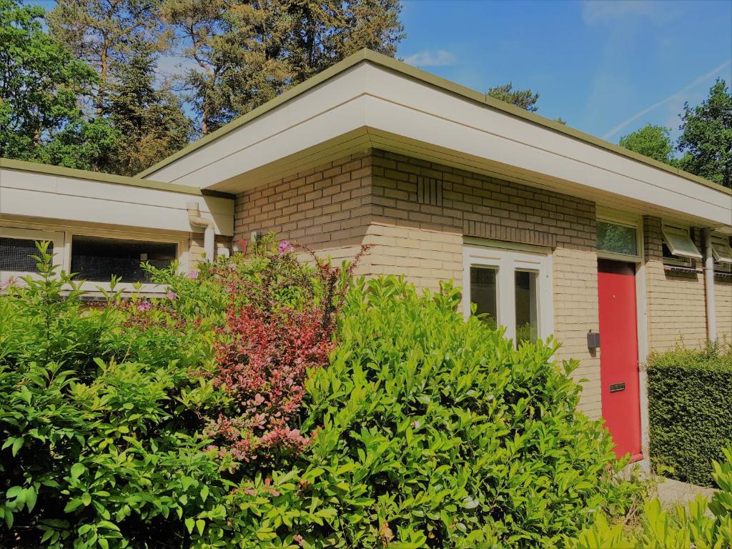 una casa con una puerta roja y algunos arbustos en Bungalow Hartje Veluwe, en Otterlo