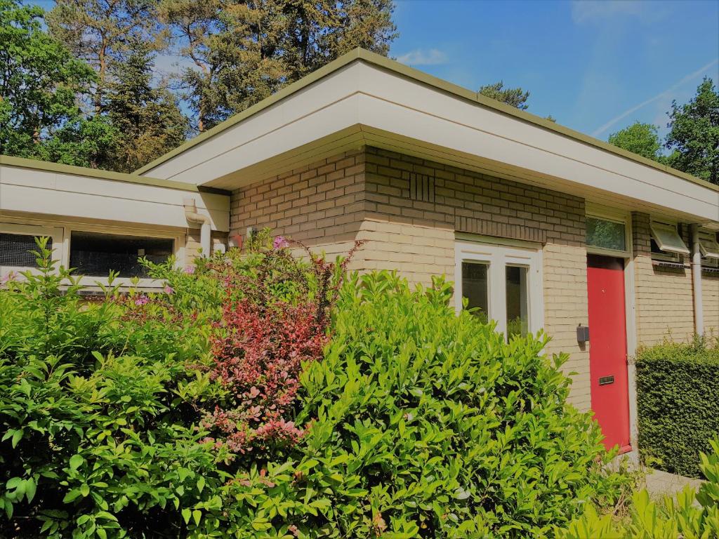 a house with a red door and some bushes at Bungalow Hartje Veluwe in Otterlo