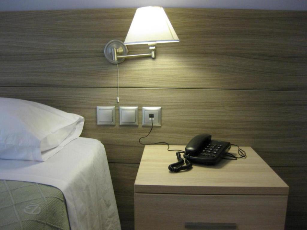 un teléfono en una mesita de noche junto a una cama en Alexandros, en Kamena Vourla