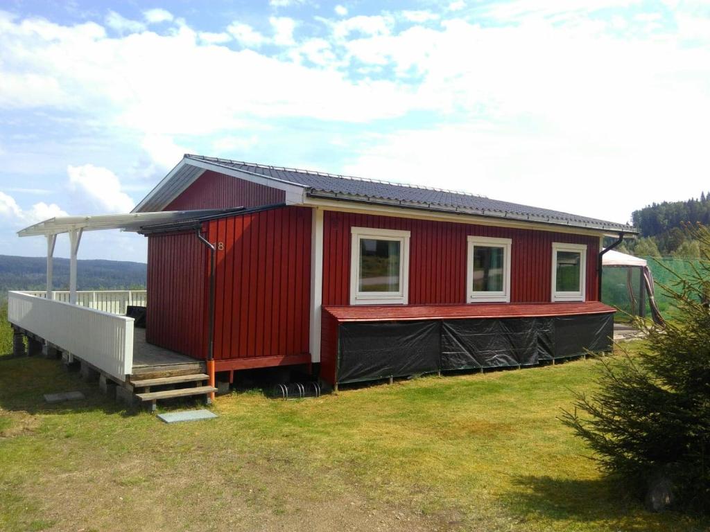 een rood huis met een veranda op een veld bij Sunne Stugcenter 18 in Gräsmark