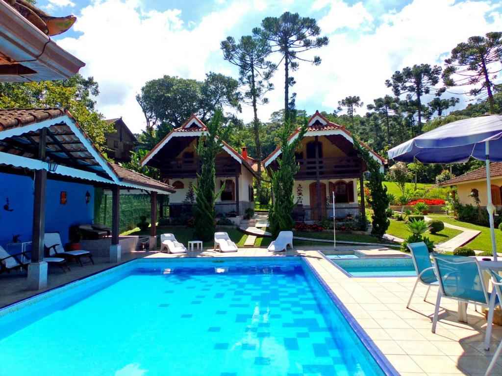 a swimming pool with chairs and a house at Hotel Cantinho de Férias in Visconde De Maua