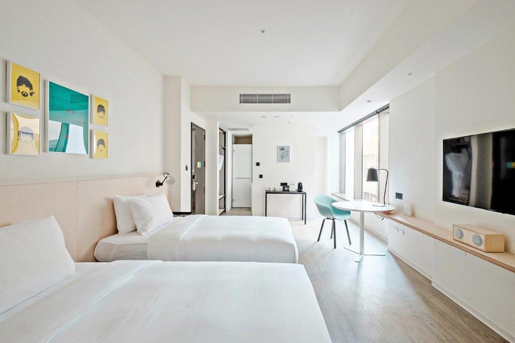 a white hotel room with two beds and a tv at amba Taipei Songshan in Taipei