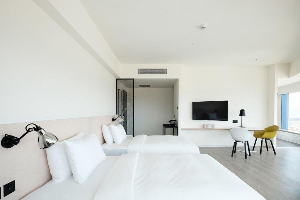 a white bedroom with two beds and a tv at amba Taipei Songshan in Taipei