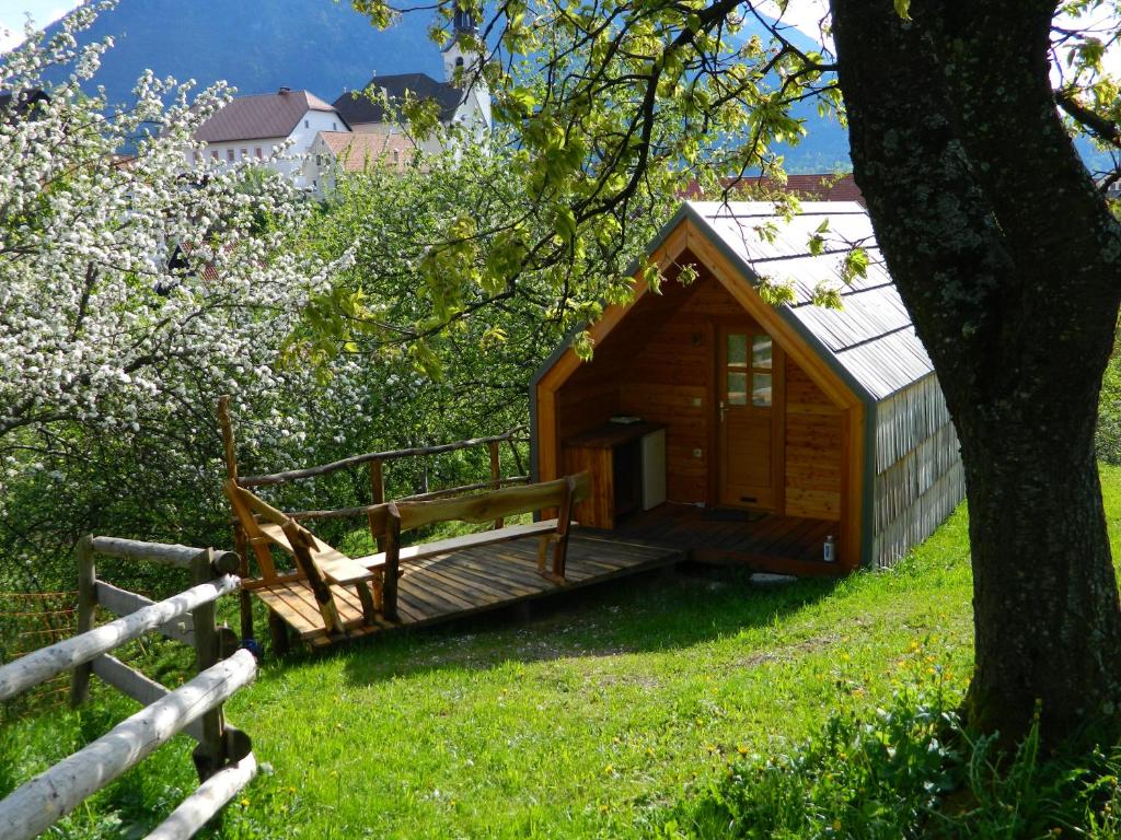 een houten hut met een veranda en een boom bij Glamping Organic Farm Slibar in Tržič