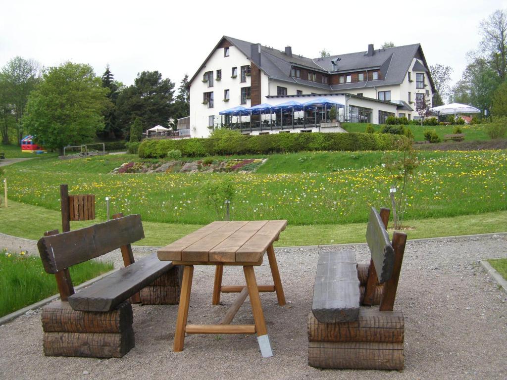 una mesa de picnic de madera y bancos frente a una casa en Hotel Waldesruh, en Lengefeld