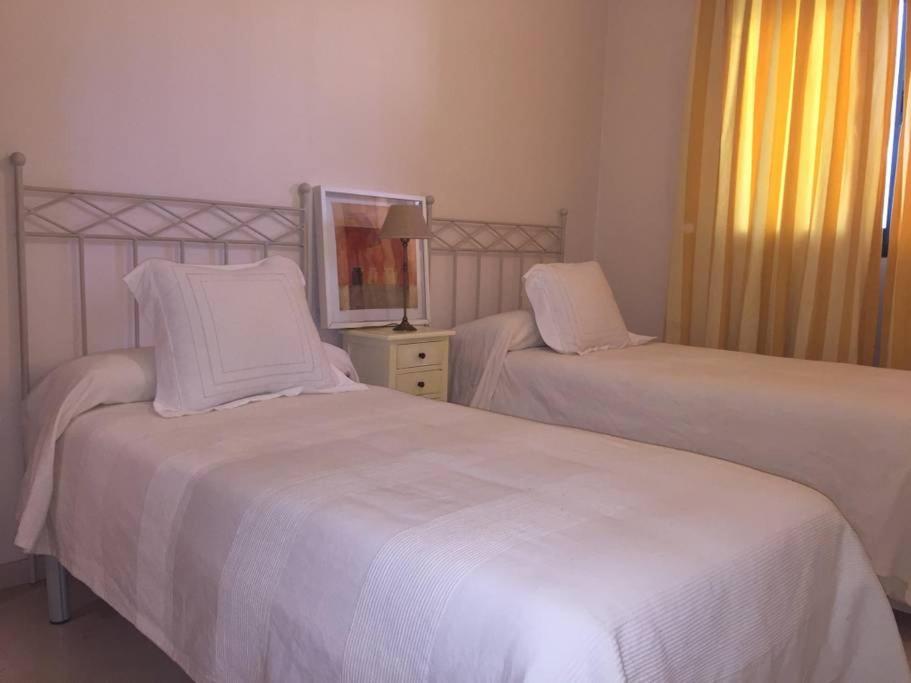 a bedroom with two beds with white sheets and a mirror at Conjunto Altos de Vista Nevada,nº11,portal 7,1ºA. in Granada