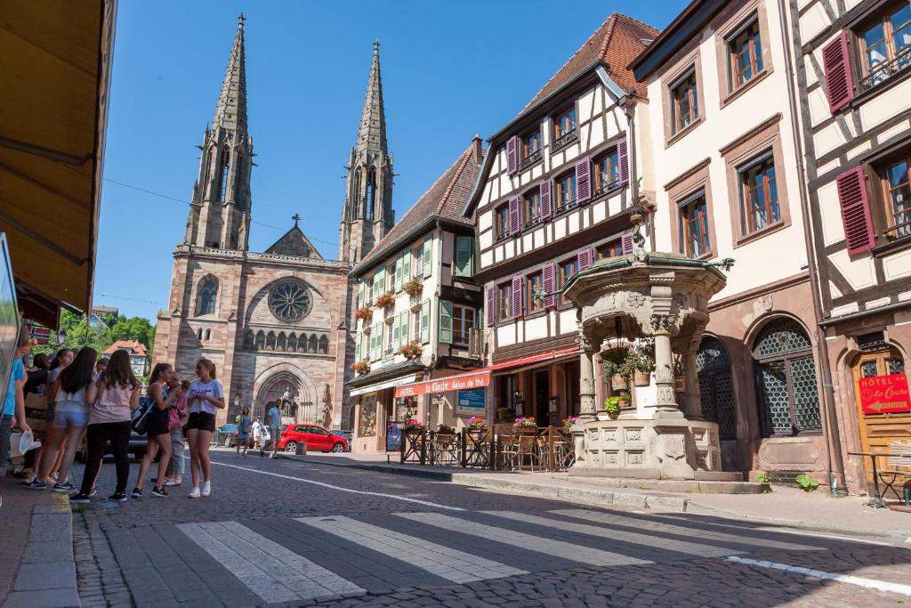 a group of people walking down a street with a church at Hôtel De La Cloche in Obernai