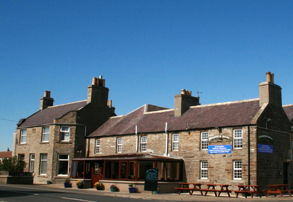 un gran edificio de ladrillo con mesas de picnic delante de él en Smithfield Hotel, en Dounby