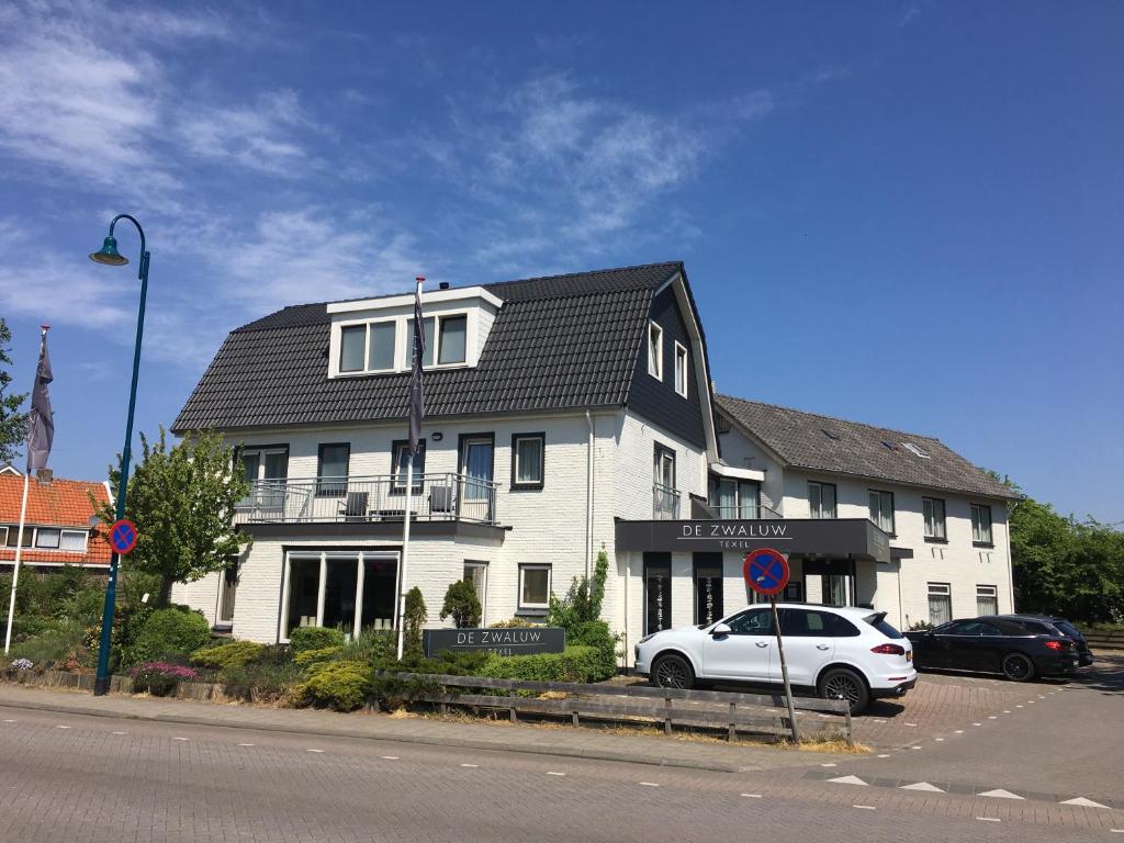 een witte auto geparkeerd voor een wit gebouw bij Boutique Hotel de Zwaluw in De Koog