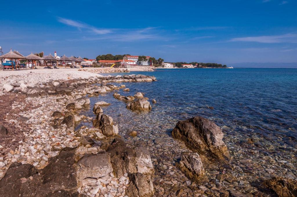 a beach with rocks in the water and houses at Apartments Cvita Ugljan in Ugljan