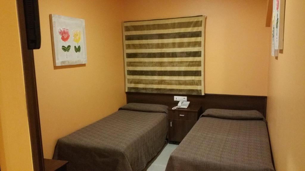 Habitación pequeña con 2 camas y ventana en Hotel León, en La Palma del Condado