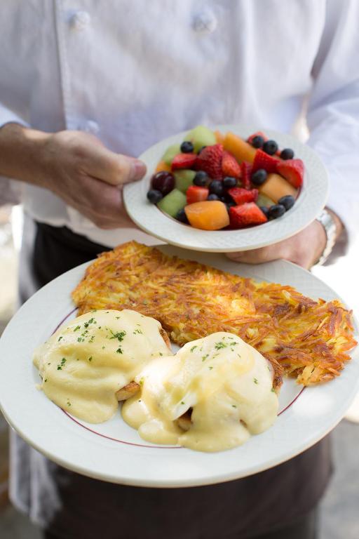 a person holding two plates of food and a bowl of fruit at Rogue Regency Inn & Suites in Medford