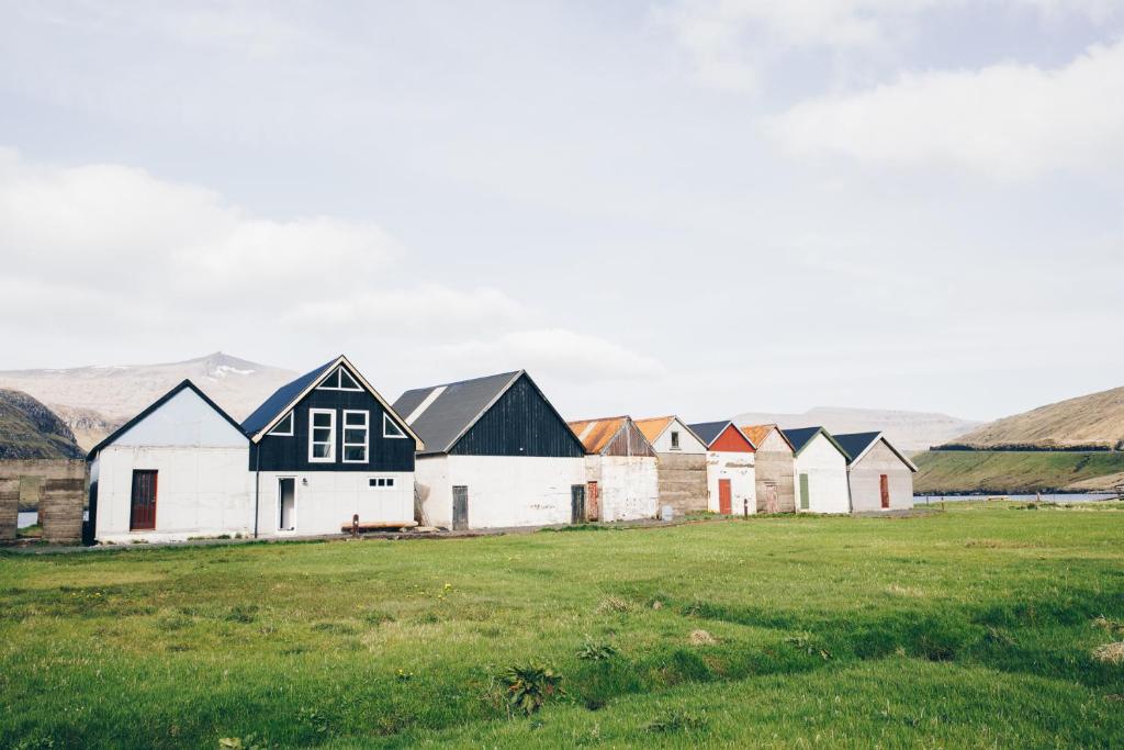 eine Gruppe von Häusern auf einem Feld mit Bergen im Hintergrund in der Unterkunft Boat house in Hósvik in Hósvík