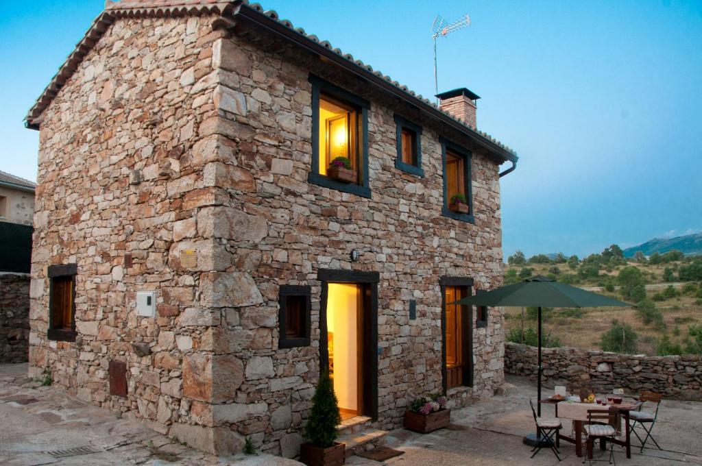 ein Steinhaus mit einem Tisch und einem Sonnenschirm in der Unterkunft AL VIENTO, Alojamiento & Turismo Rural Horcajuelo in Horcajuelo de la Sierra