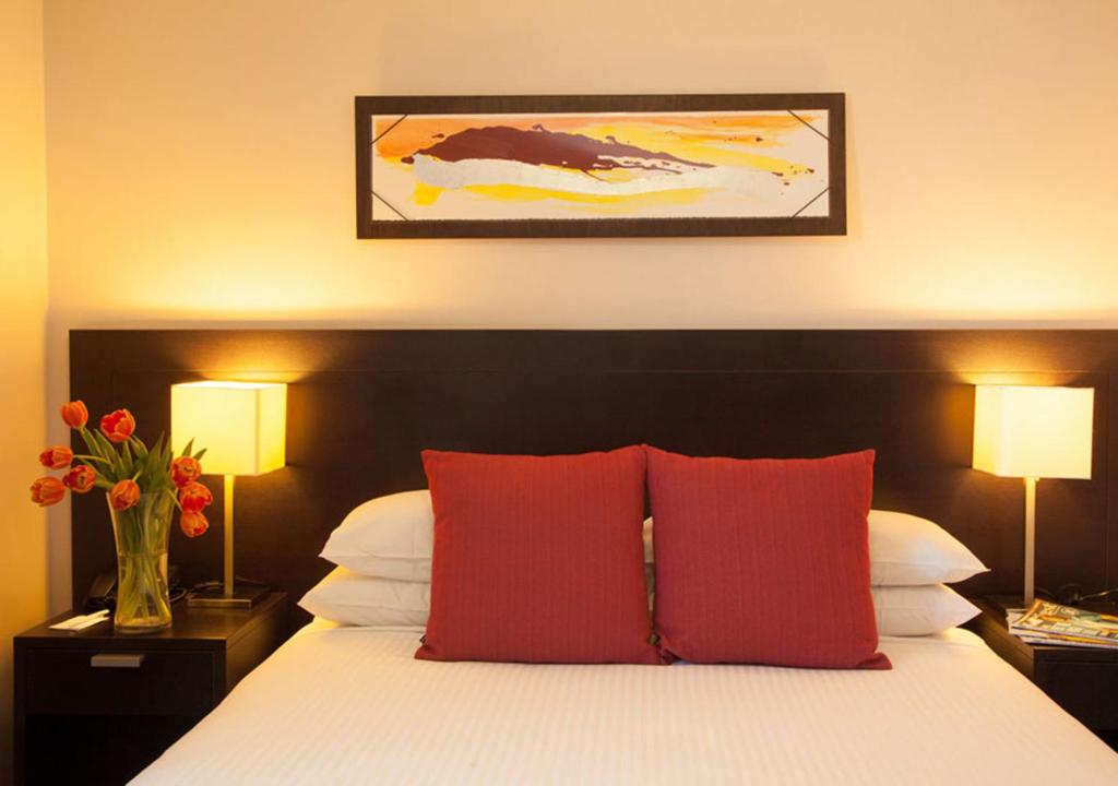 a bedroom with a bed with red pillows and two lamps at Wine Country Motor Inn in Cessnock