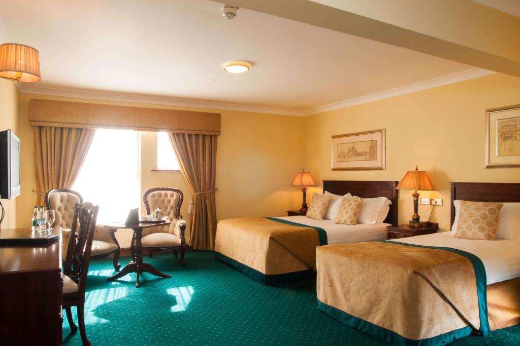 um quarto de hotel com duas camas e uma mesa e cadeiras em Meadow Court Hotel em Loughrea