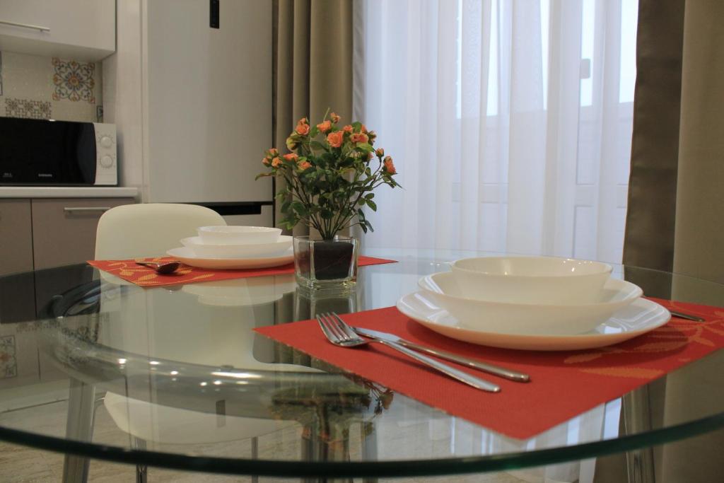 a glass table with two plates and a vase with flowers on it at Apartment Deluxe on Krasnopresnenskaya in Volgograd