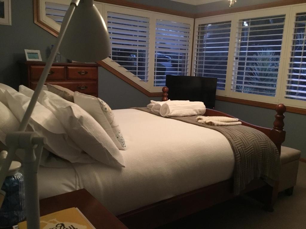 a bedroom with a bed with white sheets and windows at Kiama Guesthouse in Kiama