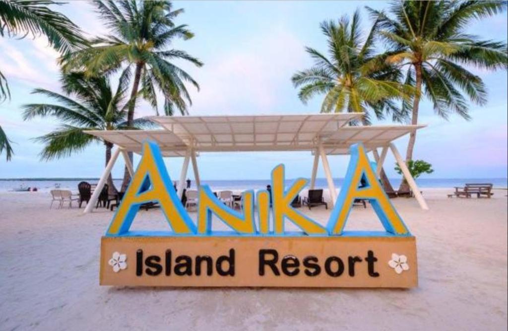 a island resort sign on a beach with palm trees at Anika Island Resort in Bantayan Island