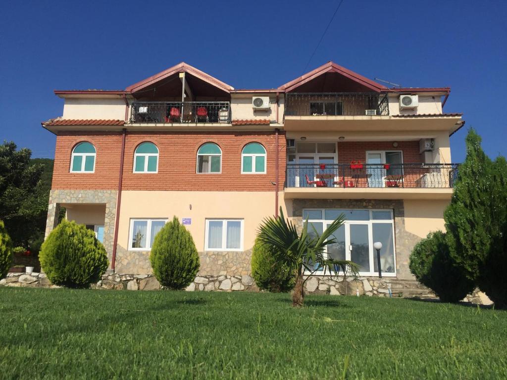 een groot huis op een heuvel met een groene tuin bij Apartmani Alex Beach in Star Dojran