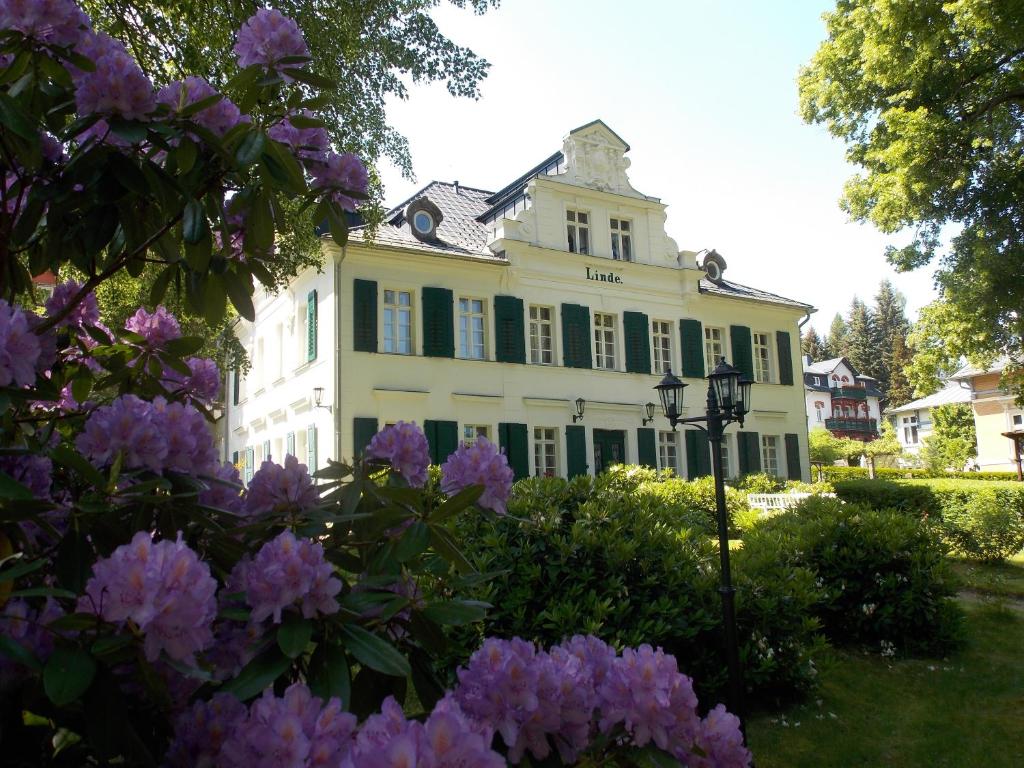 a large white house with green shutters and purple flowers at Kurheim Haus Linde in Bad Elster
