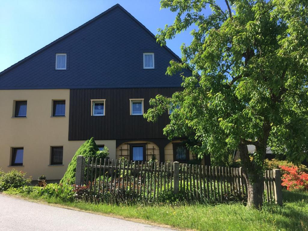ein Haus mit einem schwarzen Dach und einem Zaun in der Unterkunft Ferienwohnung Hänel in Hinterhermsdorf
