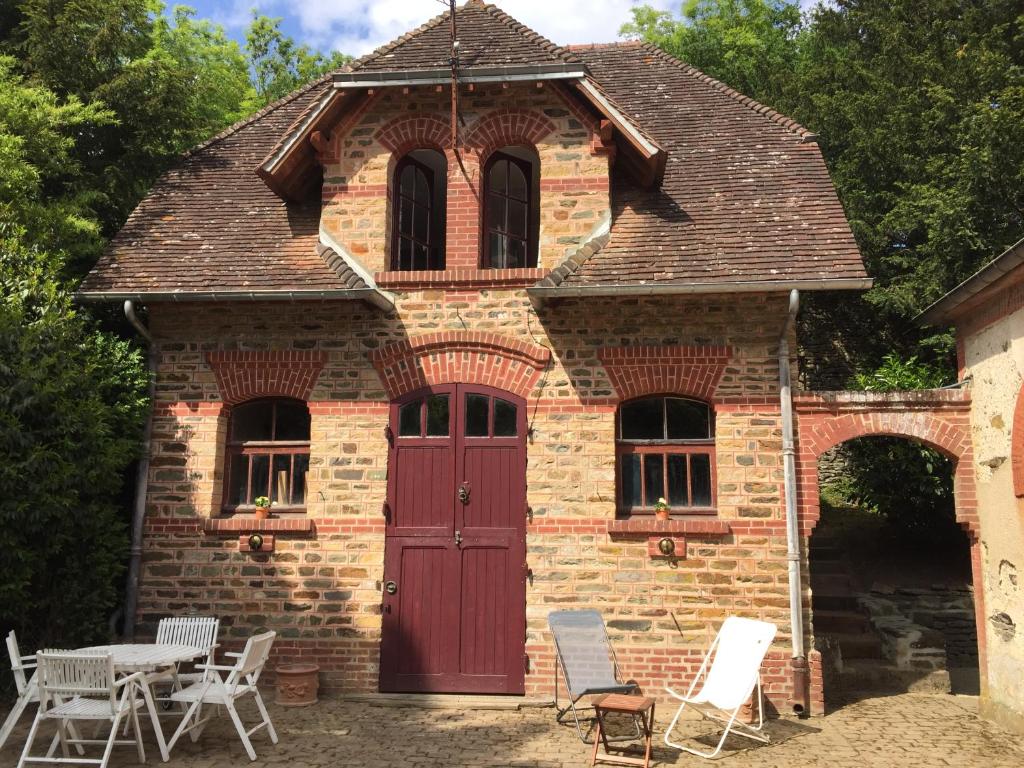 een bakstenen gebouw met een rode deur en een tafel en stoelen bij Gîte Les Ecuries du Manoir de Bénédicte in Cahan